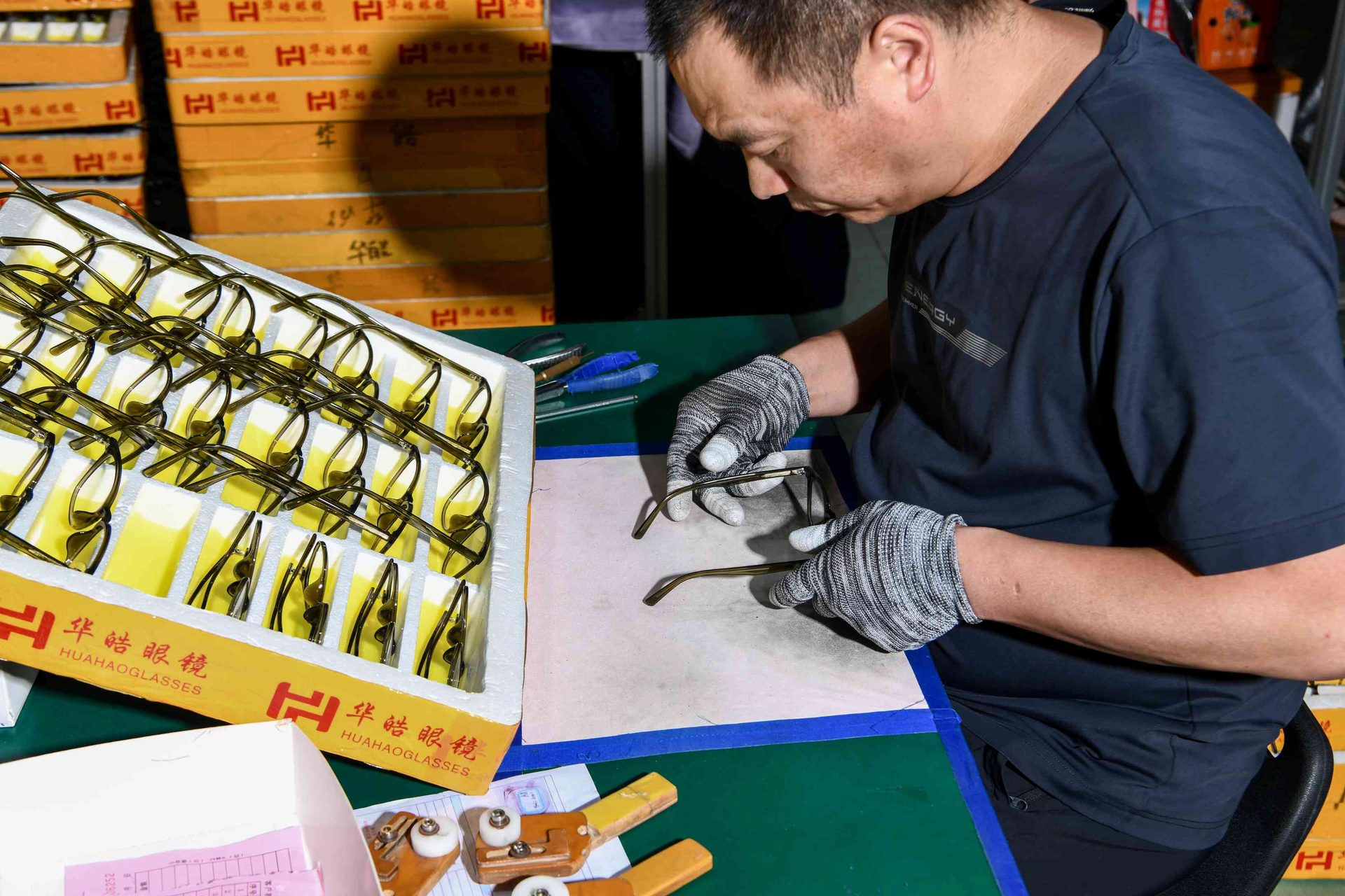 Worker hand-assembling metal optical frames beside a HAO Eyewear branded tray