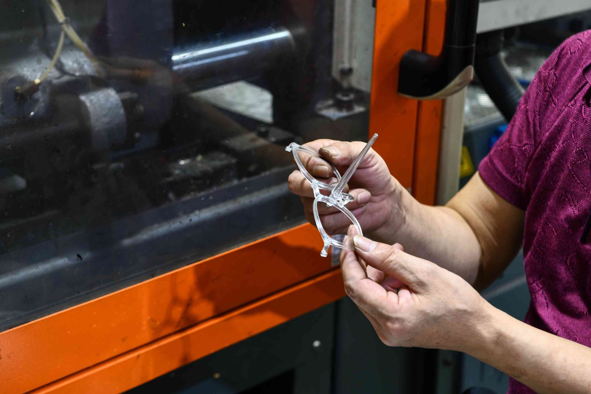 Worker holding a freshly molded transparent TR90 eyewear frame from the injection process