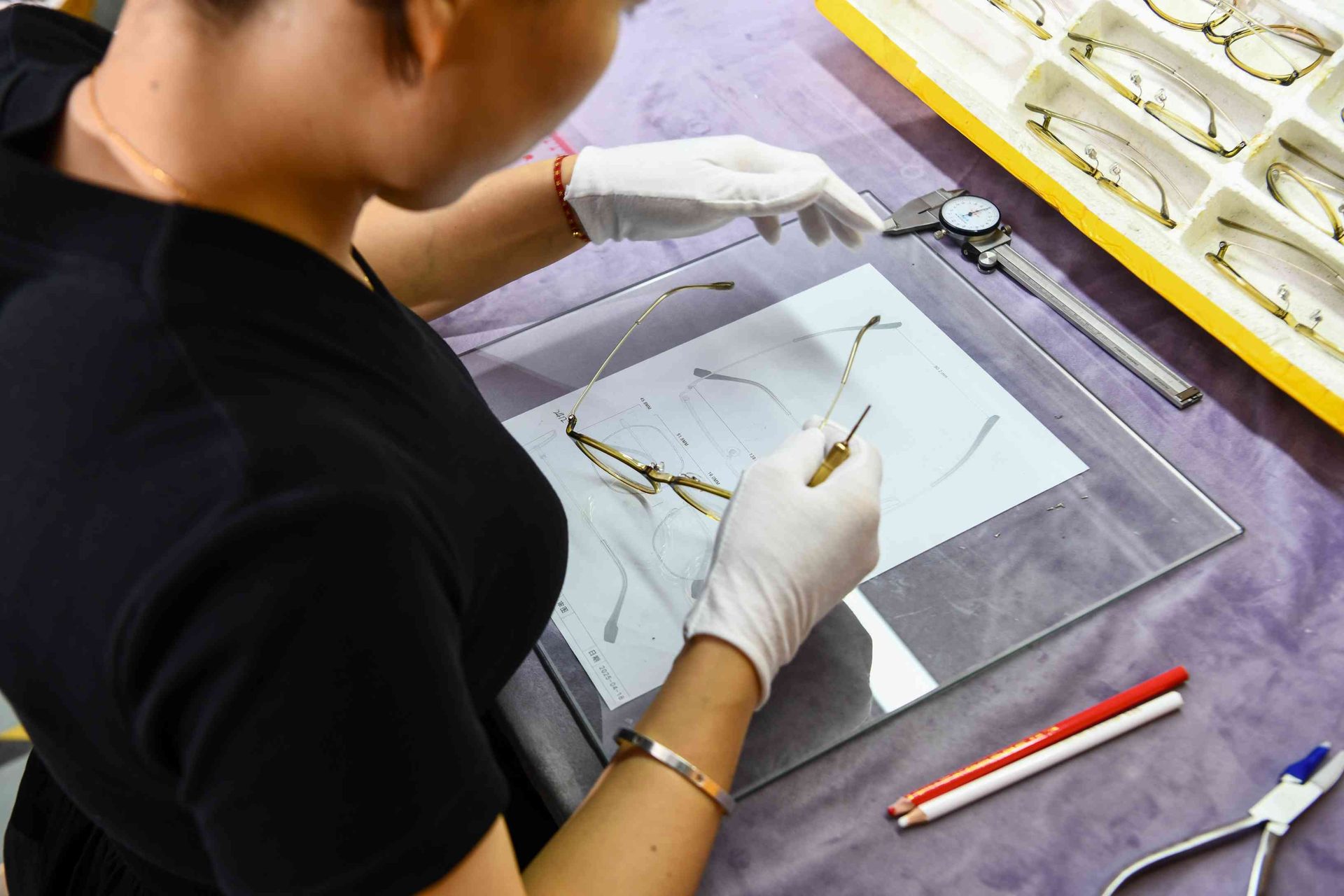 QC inspector checking eyewear frame dimensions against engineering drawings on a light table