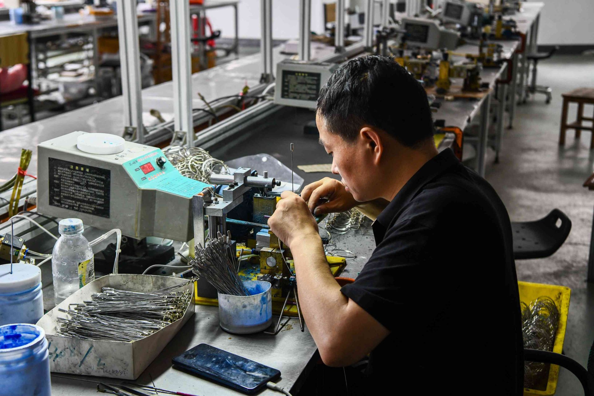Metal eyewear welding operation with extensive workshop production line in the background